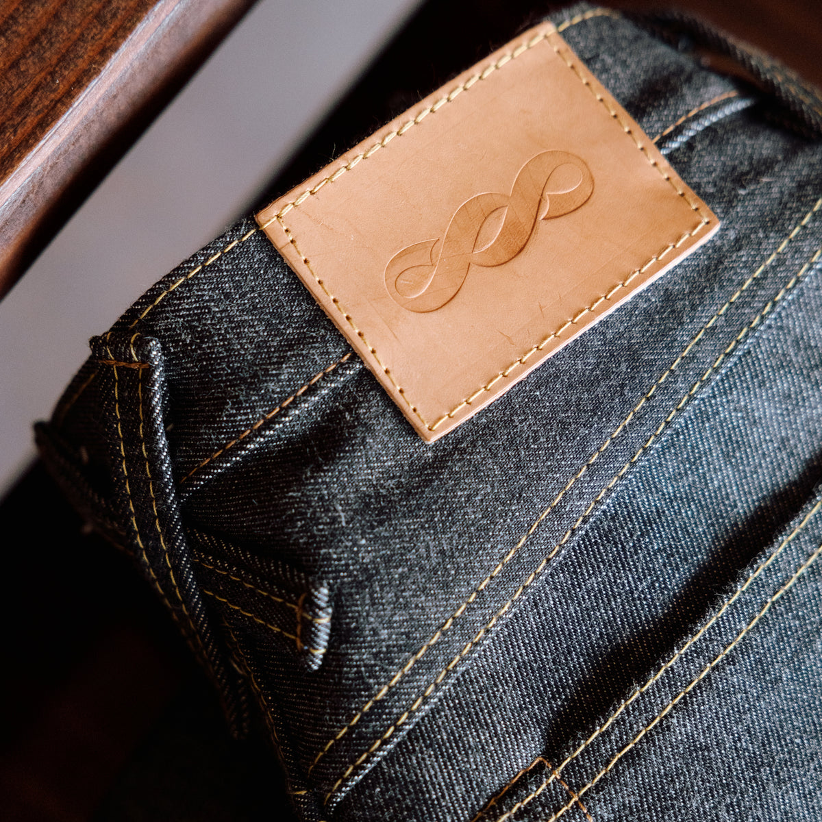 Close-up of a denim product with a brown leather label featuring a logo.
